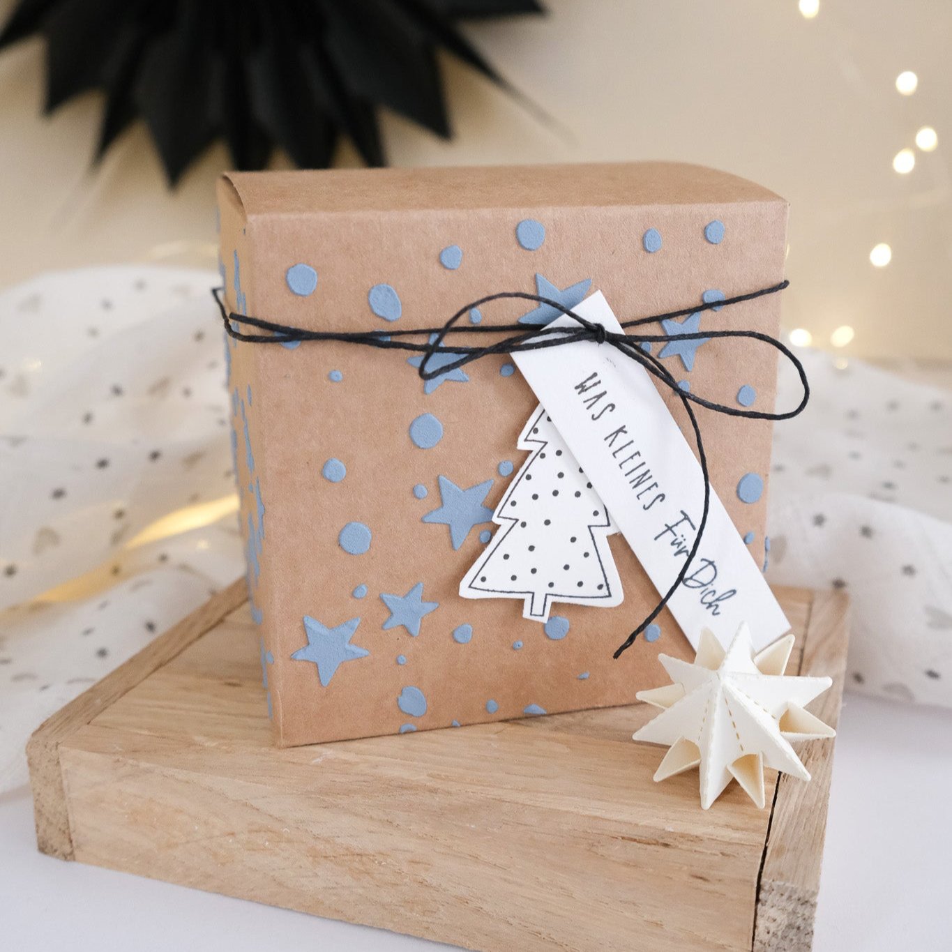 Bastelbeispiel von einer Geschenkbox in Kraftpapier mit blauer Strukturpaste verziert und kleinen weihnachtlichen Anhängern.