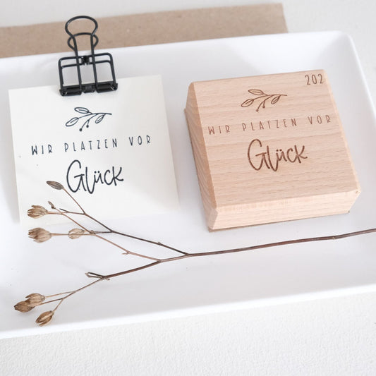 Holzstempel 5x5cm mit dem Text "Wir platzen vor Glück" und Zweig Motiv.